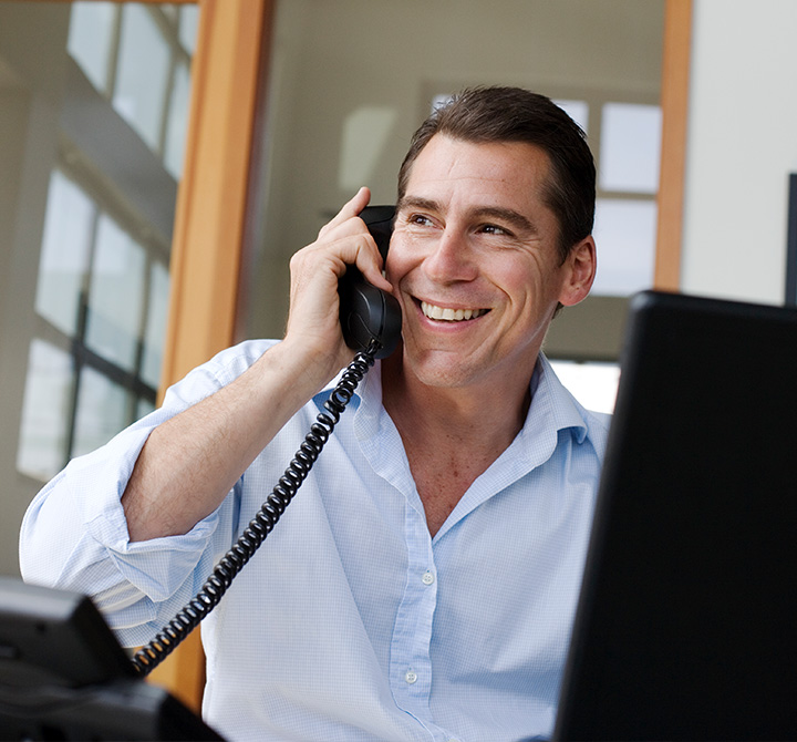 Man in office smiling while talking on a landline phone.