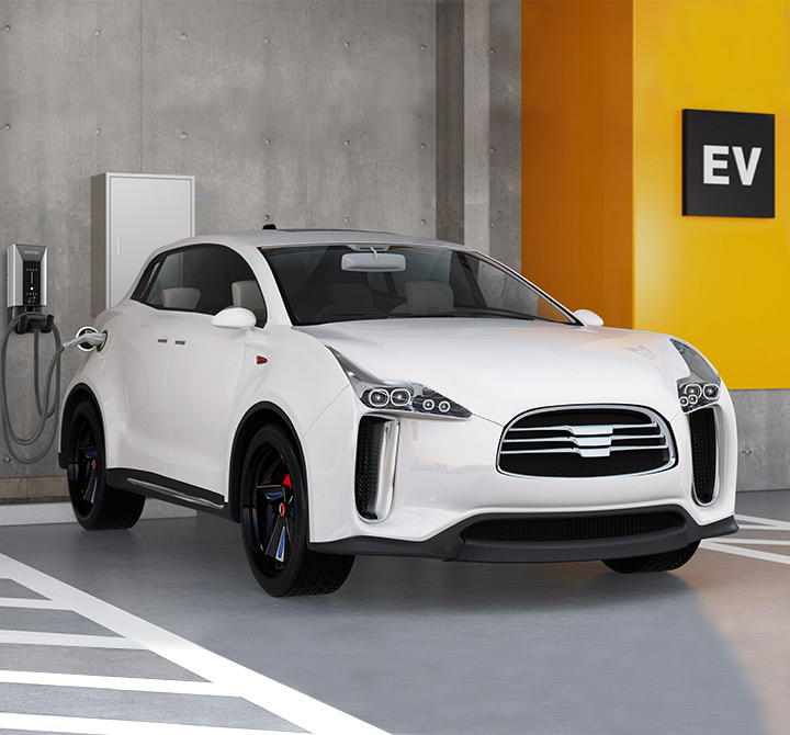 A white electric vehicle is parked in a parking garage plugged into a public vehicle charging station.